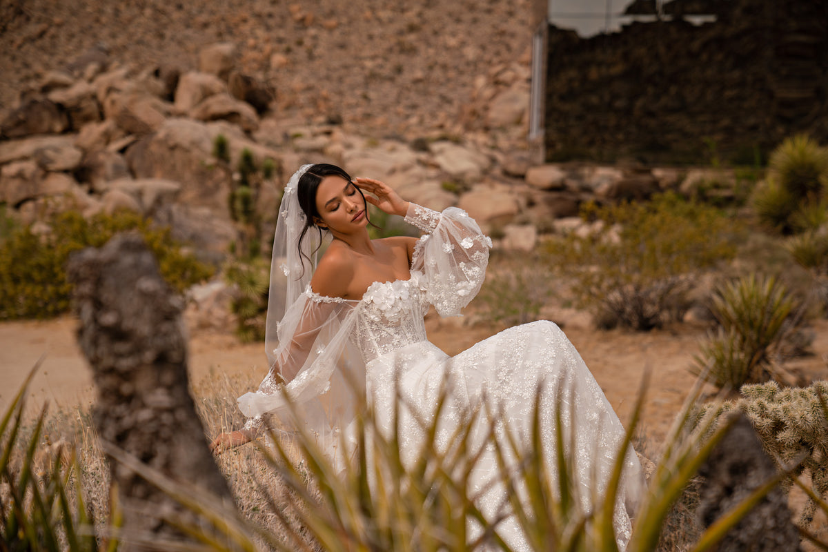 Ivory wedding dress with sheer bishop sleeves, a straight neckline, and a flowing floral-appliqué skirt