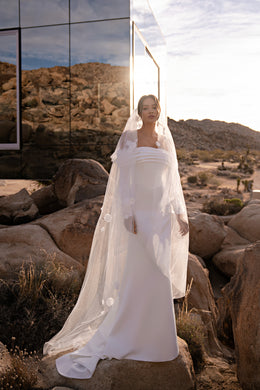 Ivory wedding dress with a draped off-the-shoulder neckline, long sleeves, fitted skirt, and train