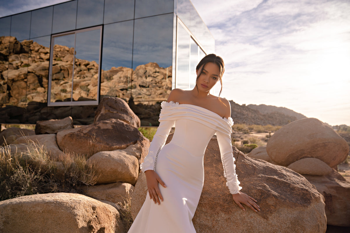 Draped off-the-shoulder neckline and fitted bodice with long sleeves on an ivory wedding dress