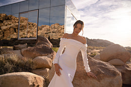 Draped off-the-shoulder neckline and fitted bodice with long sleeves on an ivory wedding dress