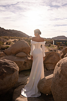 Back view of an ivory wedding dress with an off-the-shoulder back, long sleeves, fitted skirt, and train