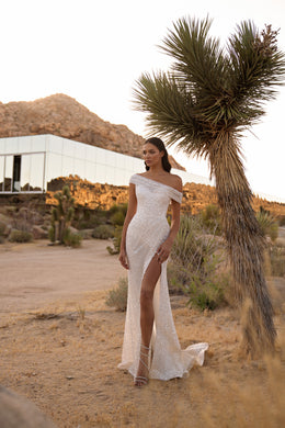 Sparkling ivory sheath wedding dress with an off-the-shoulder neckline, high slit, and short train