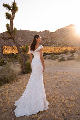 Glittering ivory wedding dress with an off-the-shoulder back, fitted sheath silhouette, and sweeping train