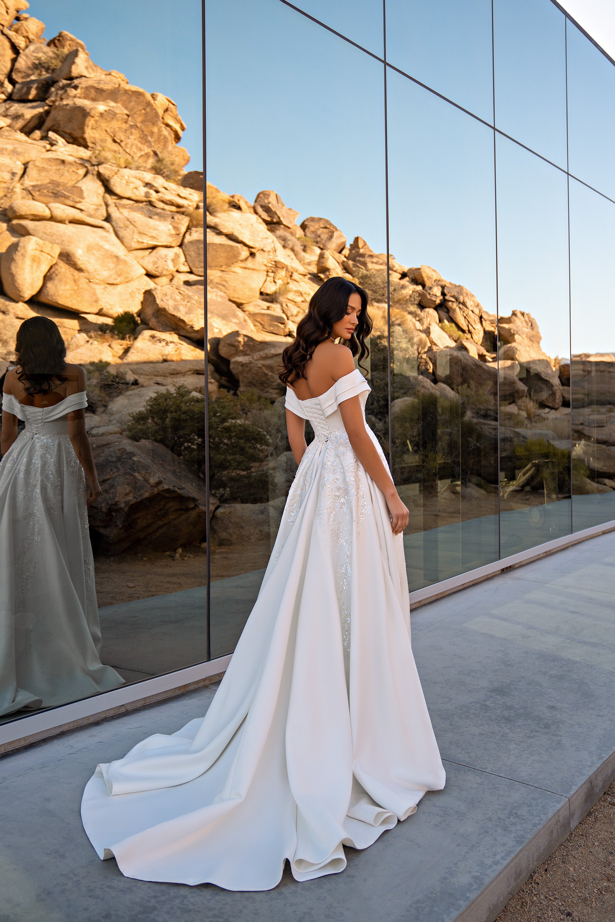 Ivory wedding dress shown from the back with off-the-shoulder sleeves, a flowing skirt, sparkling lace, and long train