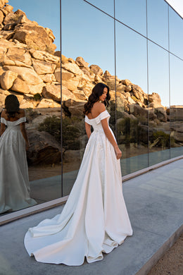 Ivory wedding dress shown from the back with off-the-shoulder sleeves, a flowing skirt, sparkling lace, and long train