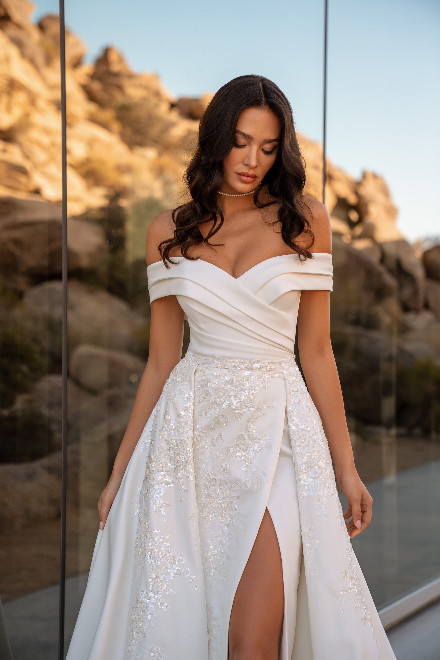 Close-up of an off-the-shoulder wedding dress with a ruched bodice, floral beadwork, and high front slit