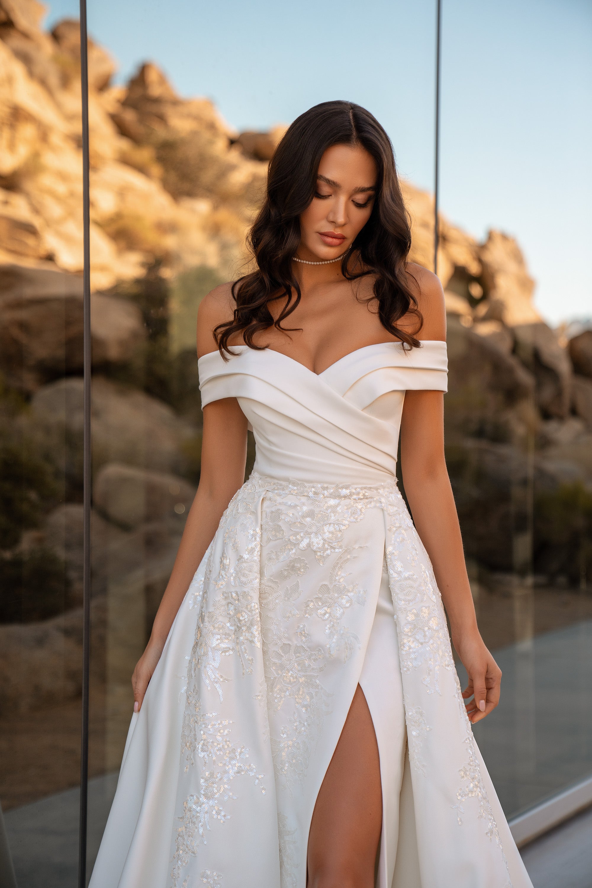 Close-up of an off-the-shoulder wedding dress with a ruched bodice, floral beadwork, and high front slit