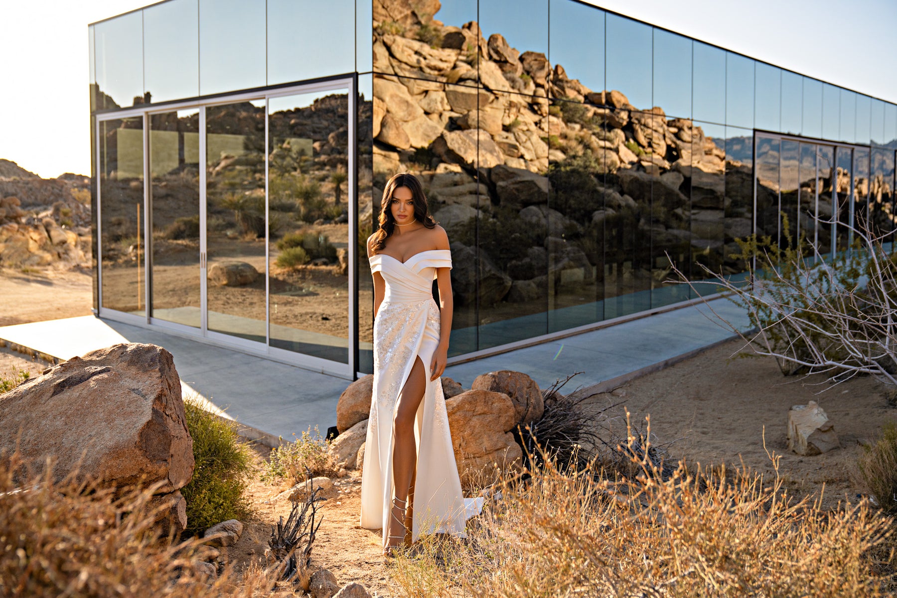 White wedding dress featuring an off-the-shoulder neckline, fitted wrap bodice, thigh-high slit, and trailing train
