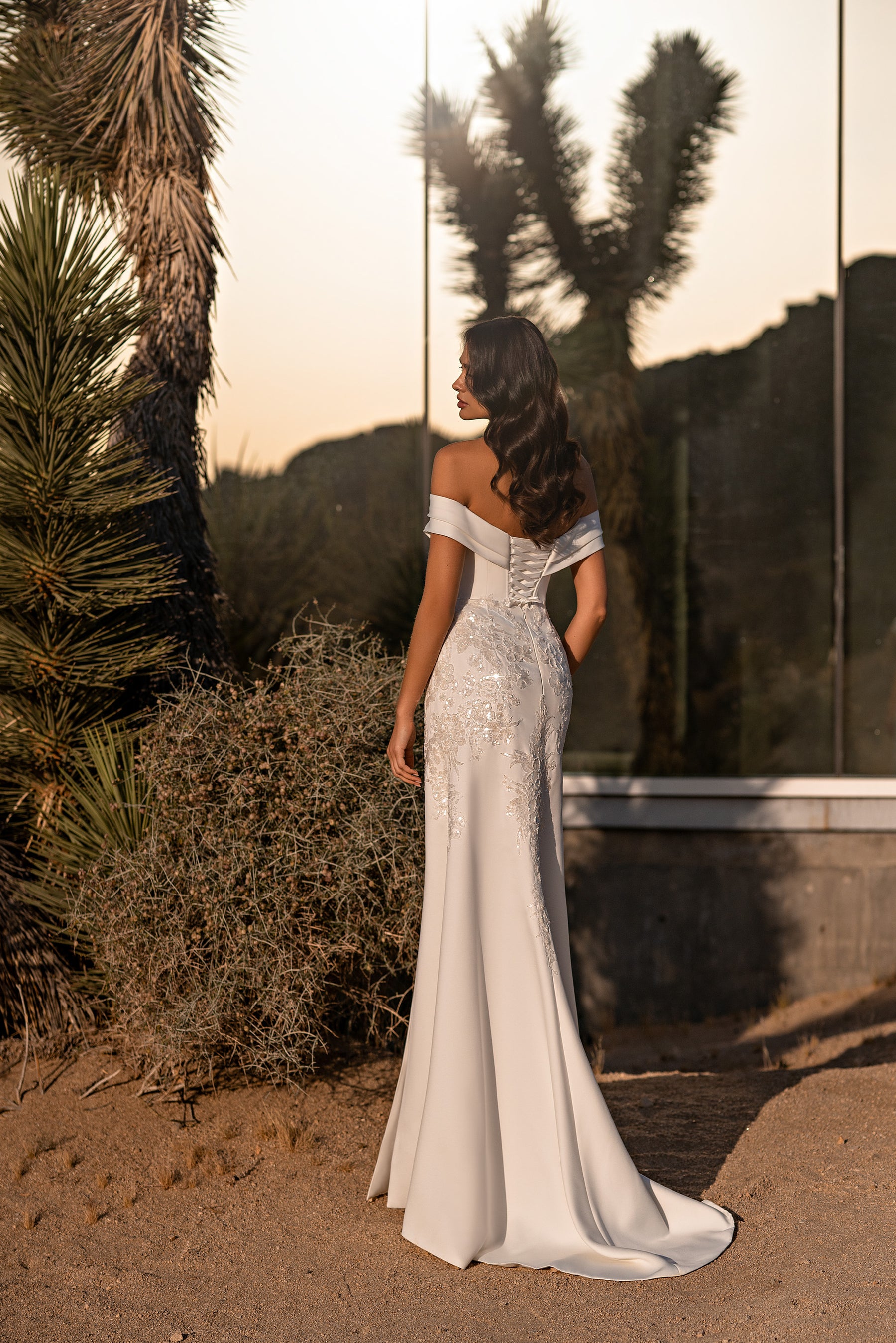 Back of an ivory wedding dress with off-the-shoulder sleeves, a sparkling embellished upper back, fitted skirt, and train