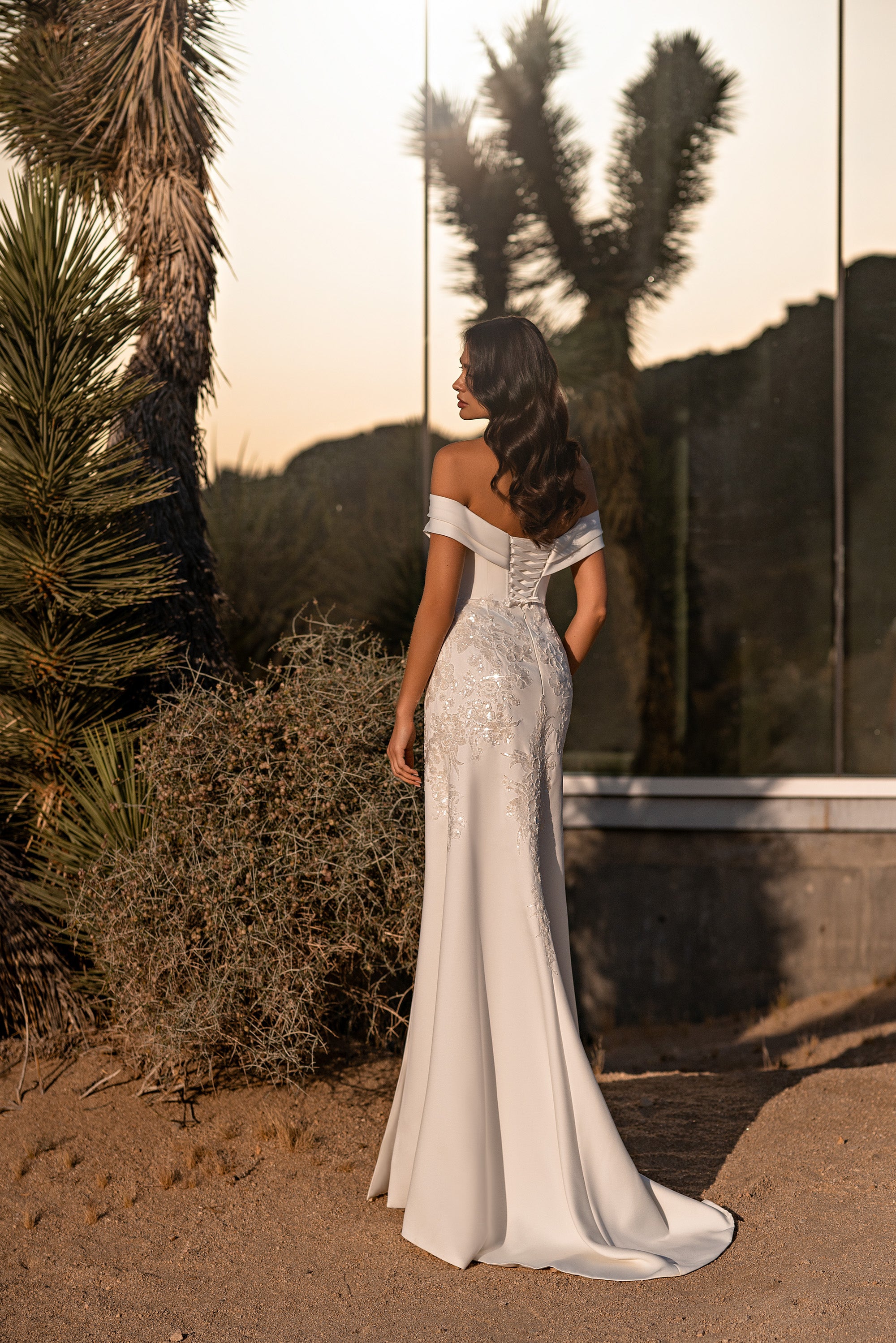 Back of an ivory wedding dress with off-the-shoulder sleeves, a sparkling embellished upper back, fitted skirt, and train