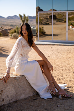Ivory wedding dress with a lace bodice, sheer long sleeve, draped skirt, and high slit