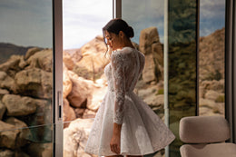 Back view of a white wedding dress with a high back, long lace sleeves, and flared mini skirt