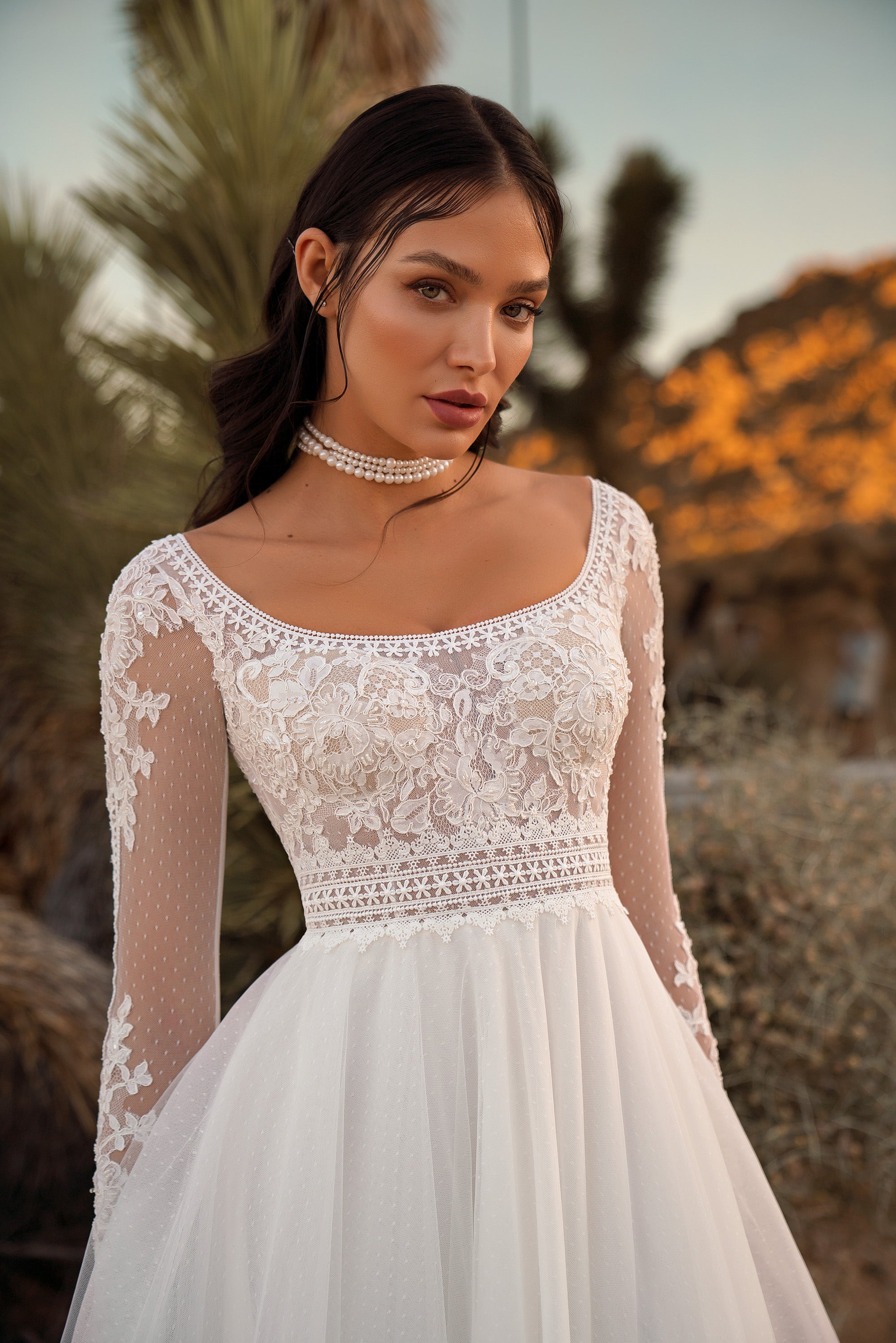 Close-up of an ivory wedding dress with floral lace bodice, scoop neckline, sheer sleeves, and textured waist