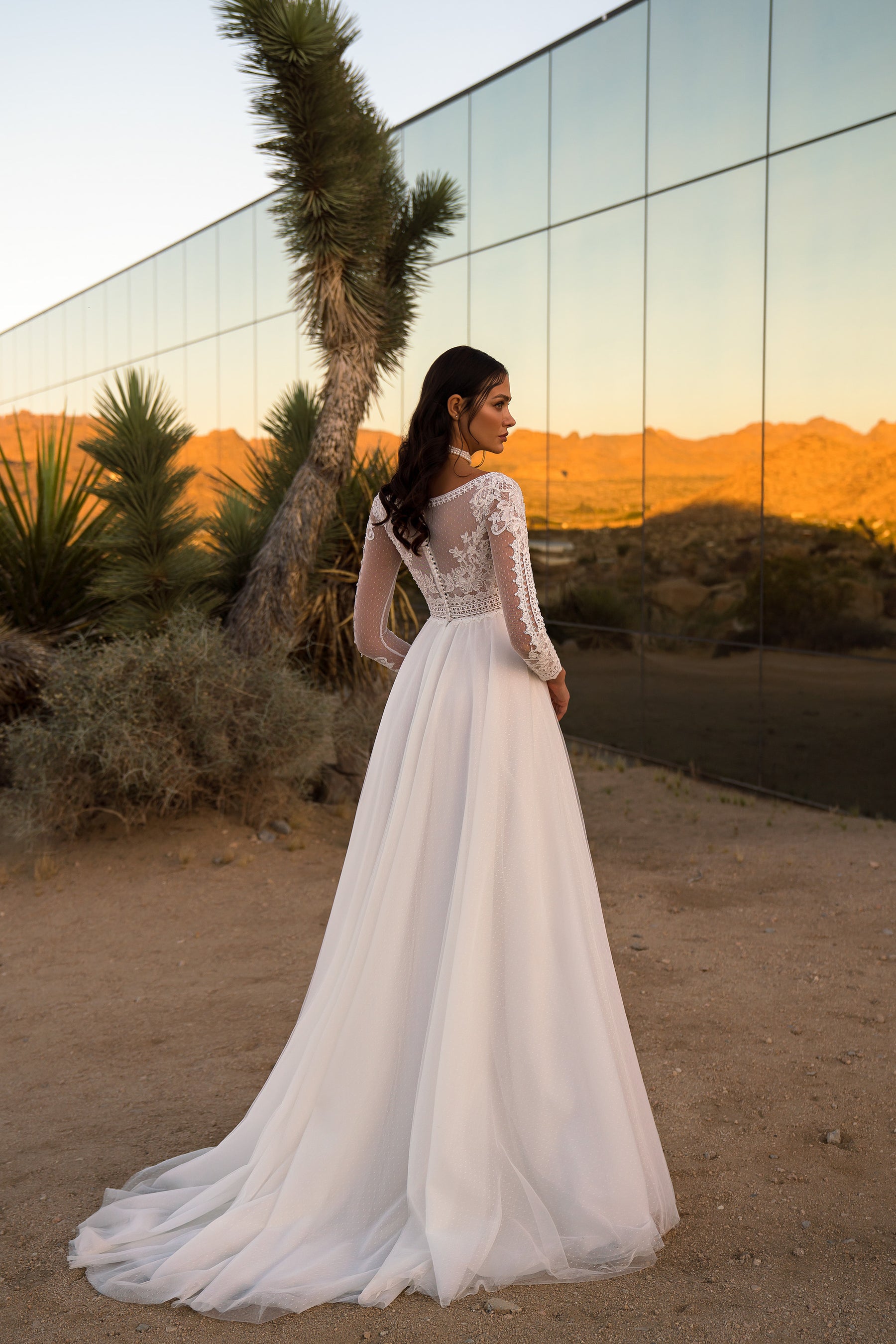 Ivory wedding dress with a sheer lace back, long sleeves, flowing A-line skirt, and sweeping train