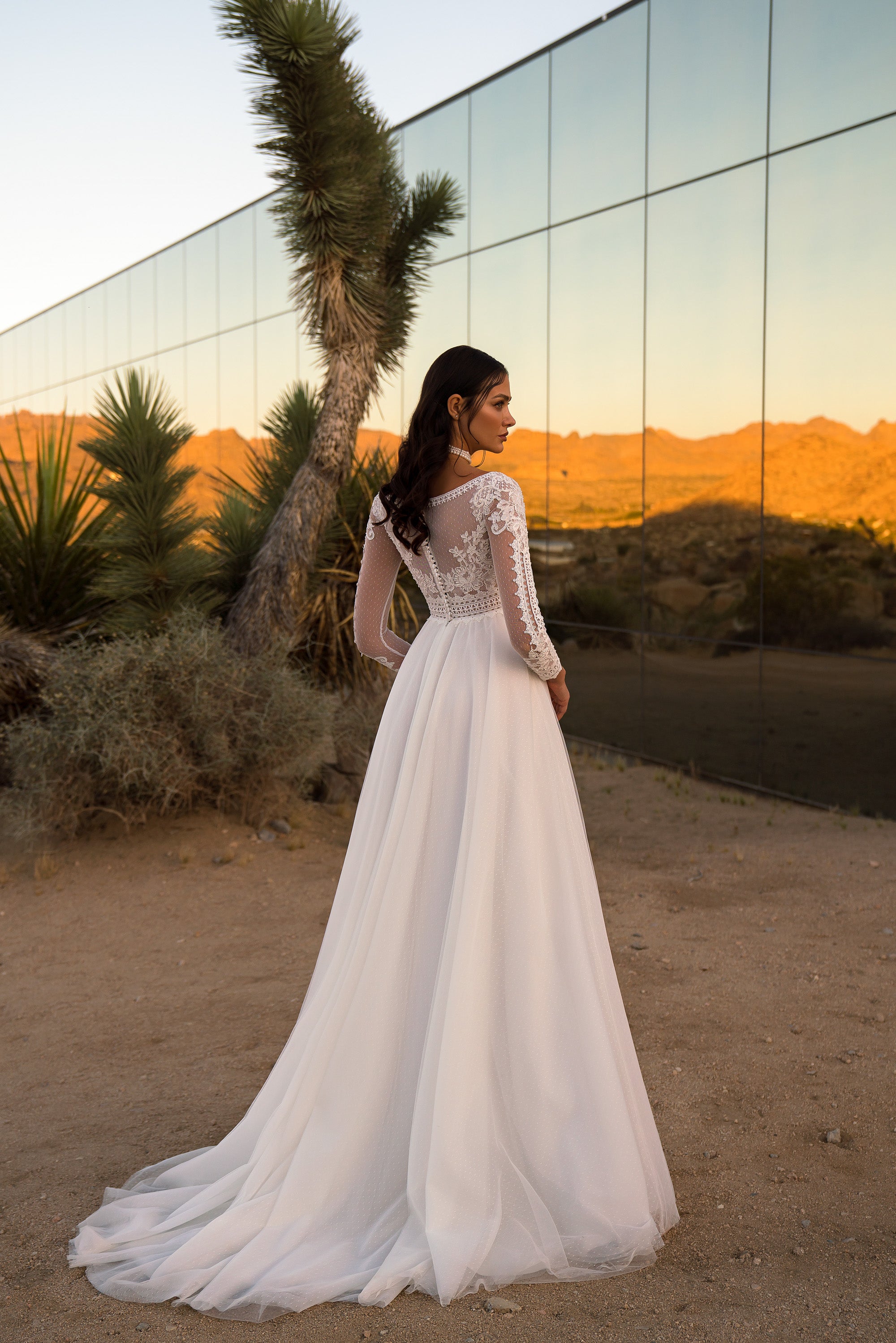 Ivory wedding dress with a sheer lace back, long sleeves, flowing A-line skirt, and sweeping train