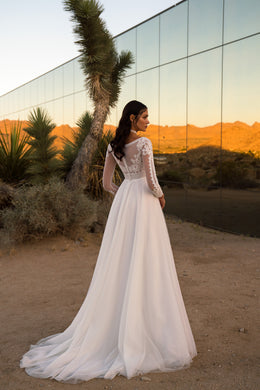 Ivory wedding dress with a sheer lace back, long sleeves, flowing A-line skirt, and sweeping train