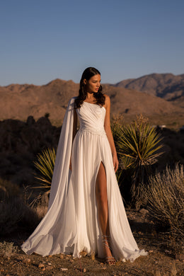 Ivory one-shoulder A-line wedding dress with a thigh-high slit and flowing draped cape