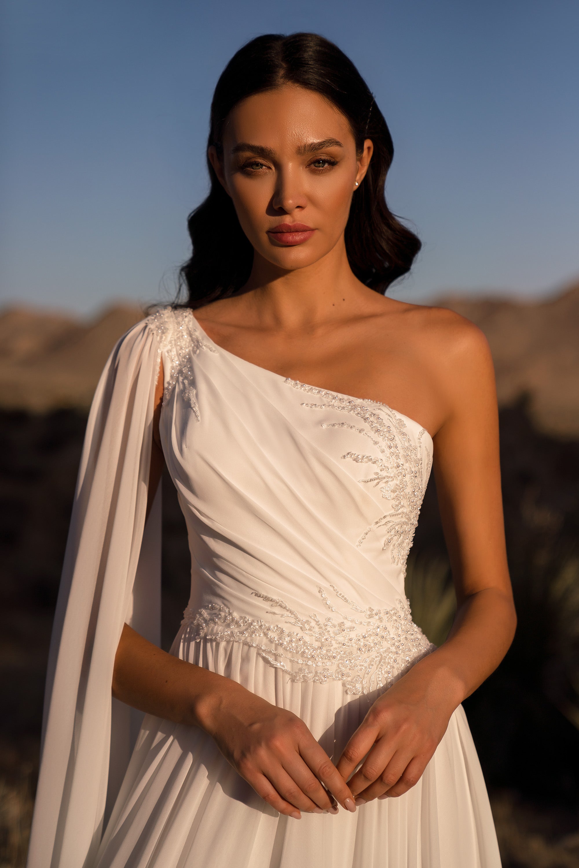 Close-up of an ivory wedding dress with a draped one-shoulder neckline and sparkling embellishment