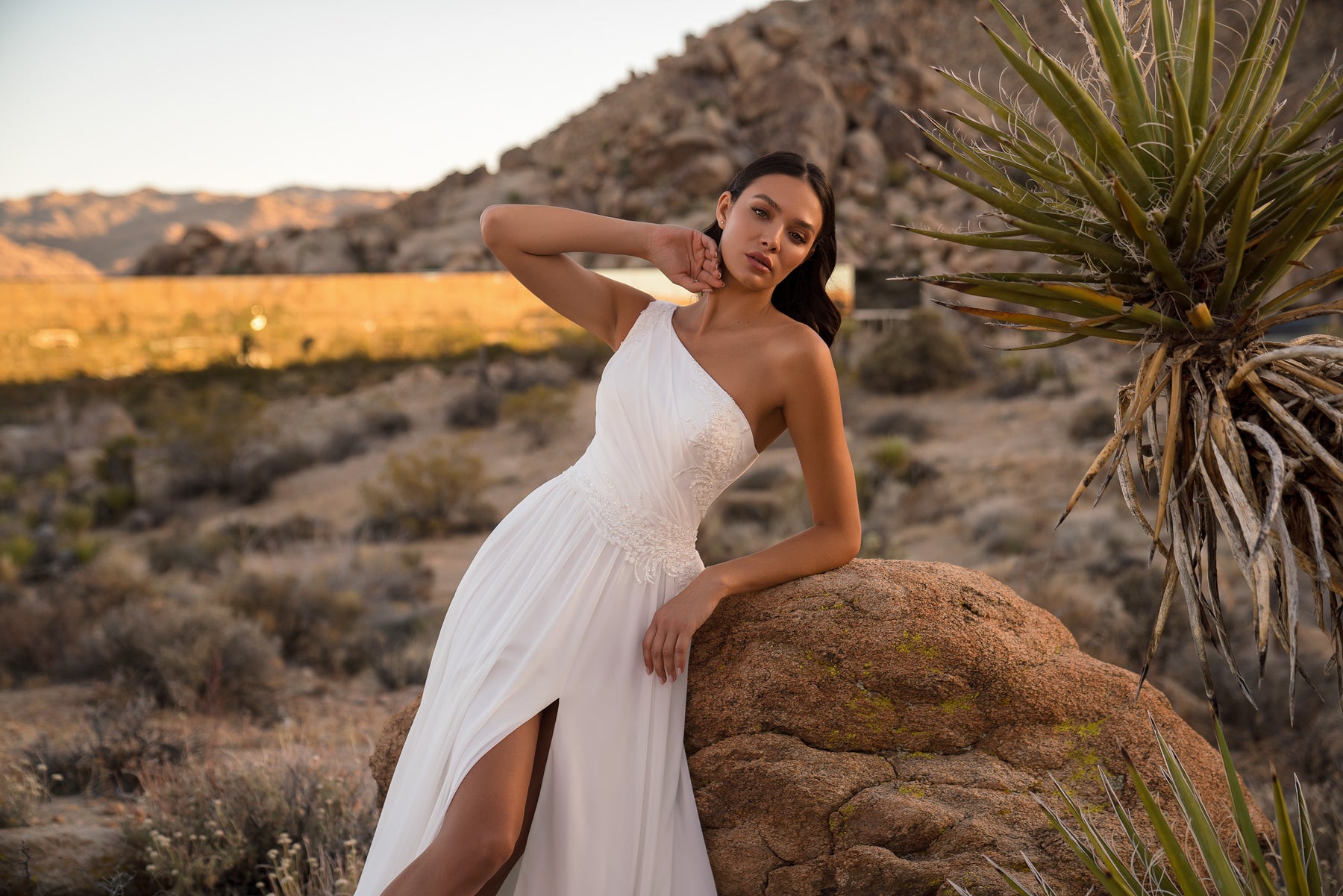 Ivory one-shoulder wedding dress with a beaded bodice, flowing skirt, and high front slit