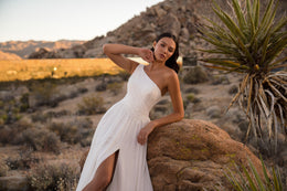 Ivory one-shoulder wedding dress with a beaded bodice, flowing skirt, and high front slit