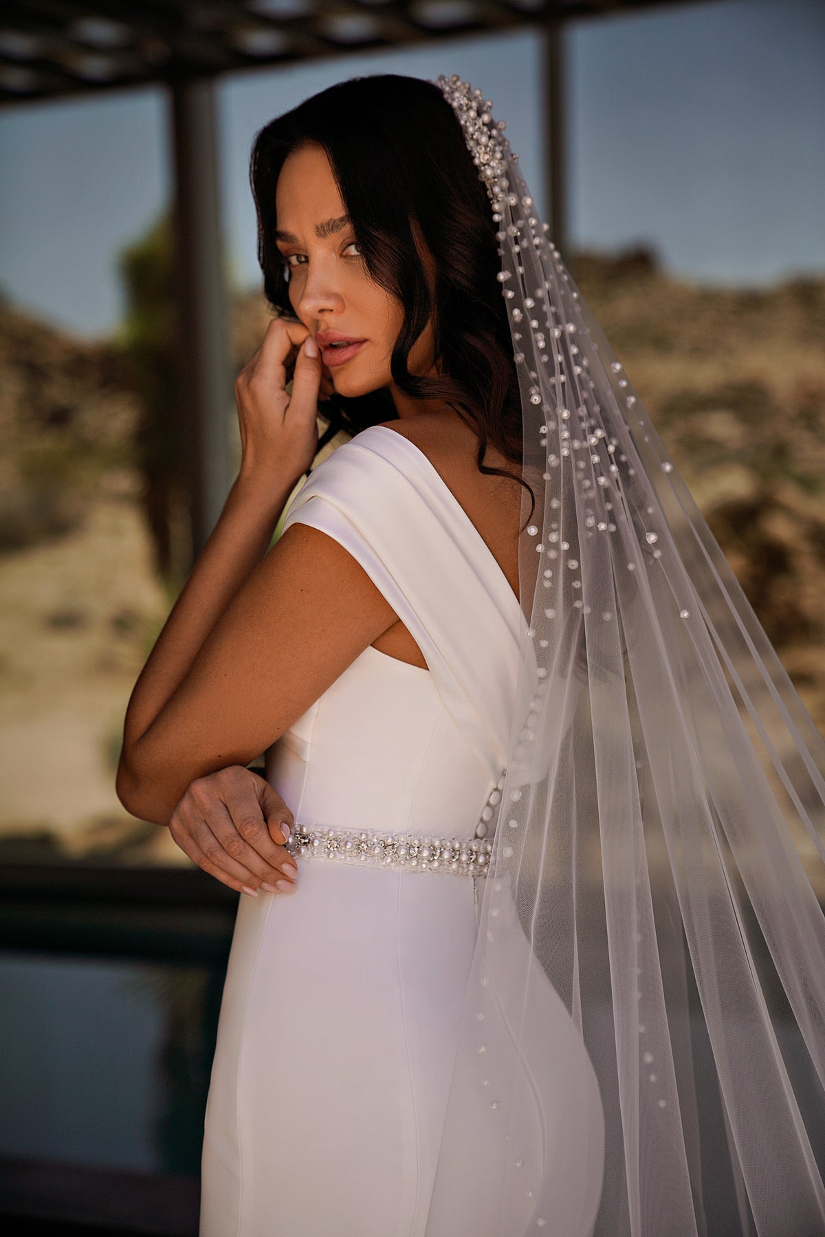 White wedding dress with a draped off-the-shoulder neckline, jeweled waist, and dotted veil