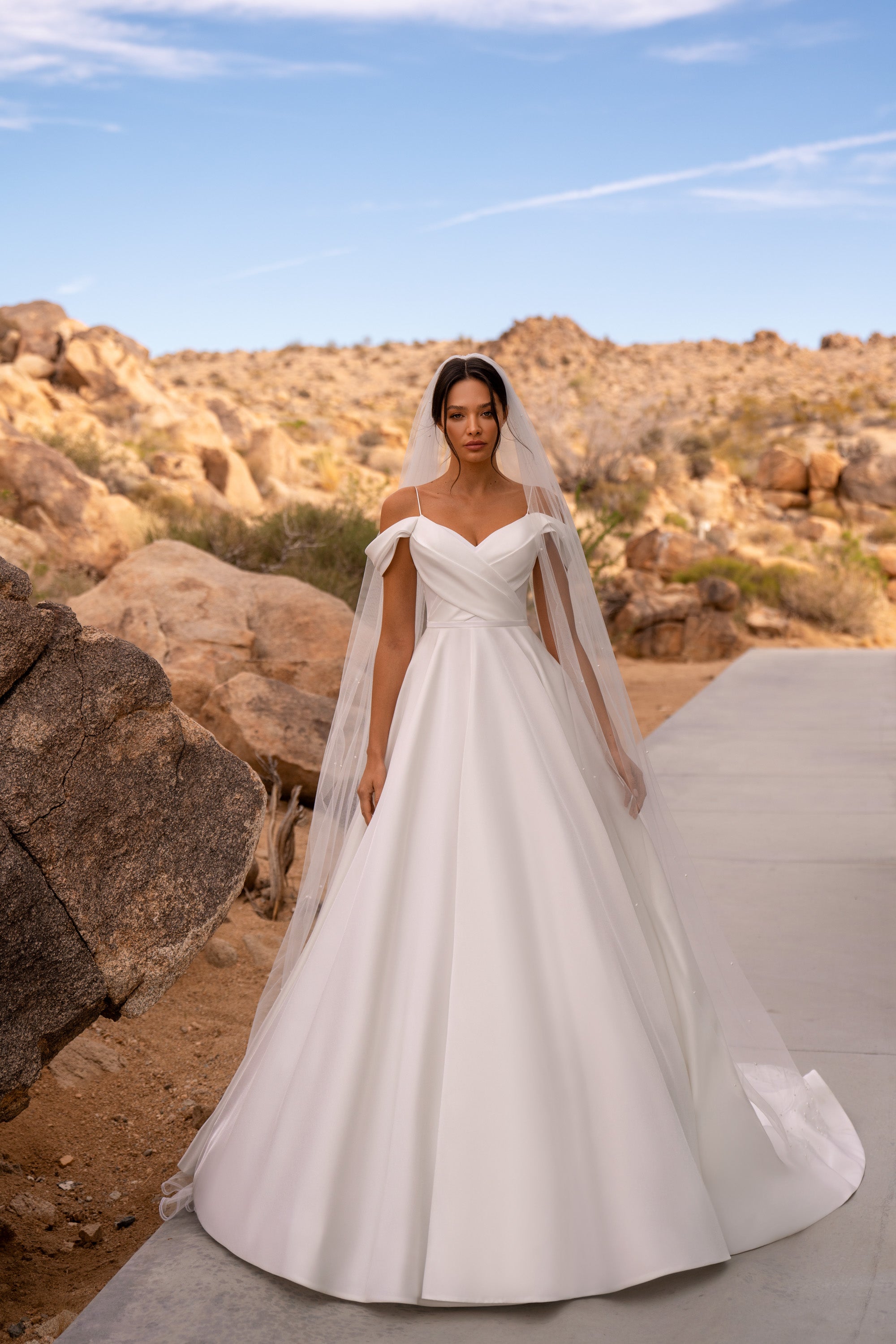 White A-line wedding dress with a draped off-the-shoulder neckline, fitted bodice, and full flowing skirt
