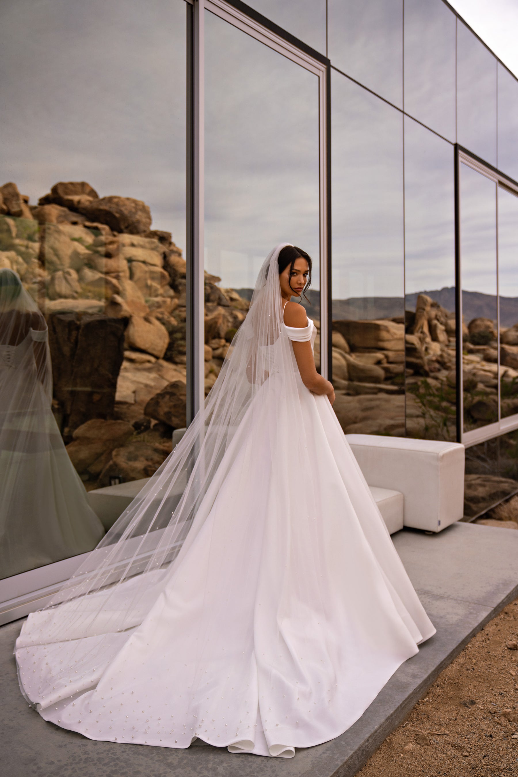 White wedding dress with off-the-shoulder sleeves, a full skirt, and a long trailing train seen from the back