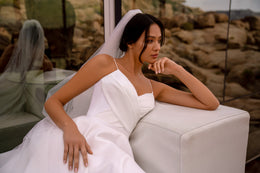 Close-up of a white wedding dress bodice with slim straps, a square neckline, and softly draped fabric