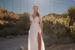 Ivory wedding dress featuring a plunging neckline, floral lace sleeves, fitted waist, and high slit