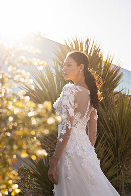 Close-up of the lace-covered back and sheer sleeves on an ivory wedding dress with a flowing train