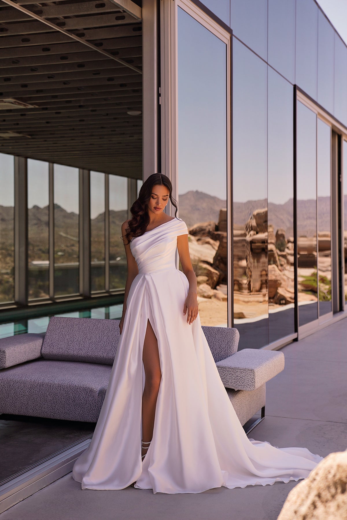 White satin A-line wedding dress with an asymmetric draped neckline, thigh-high slit, and sweeping train