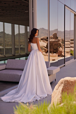 White wedding dress with a low open back, thin shoulder straps, flowing A-line skirt, and long train