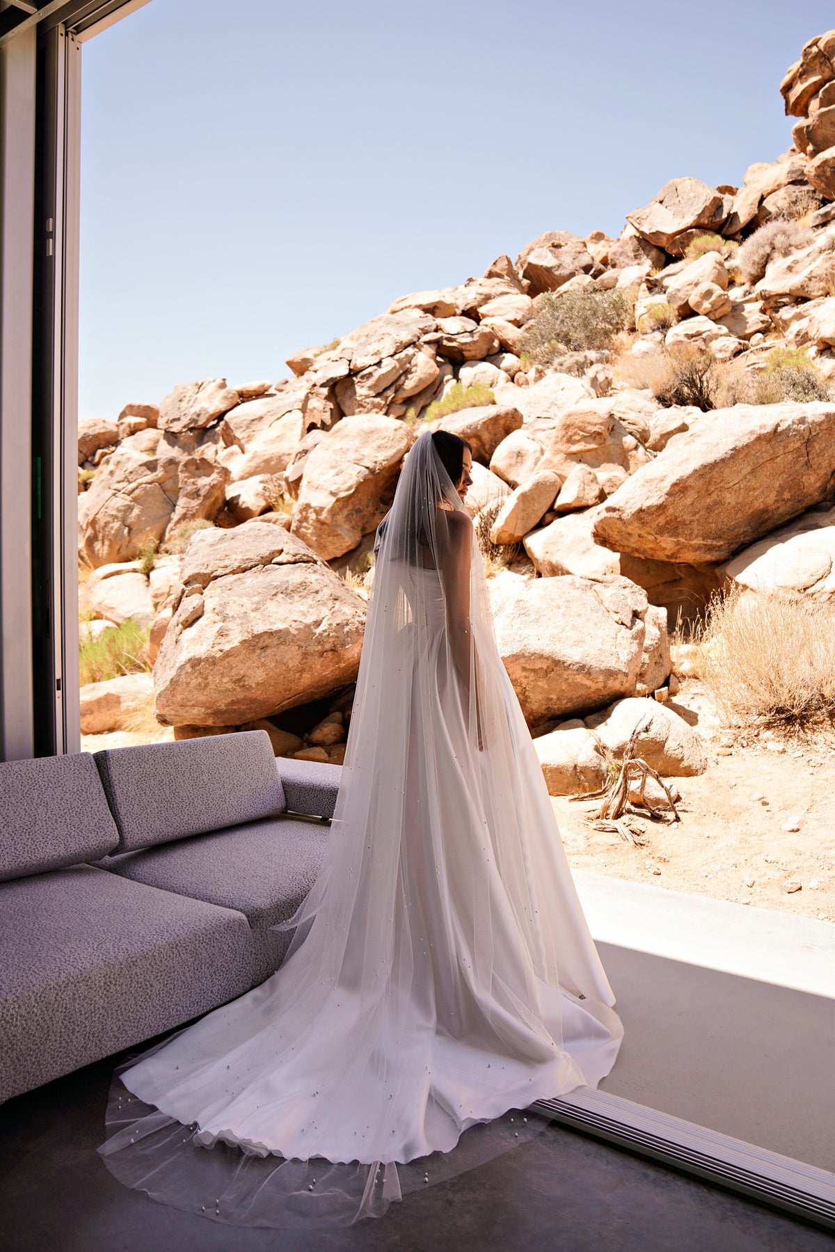 White wedding dress with a long flowing train and softly gathered floor-length skirt, viewed from behind