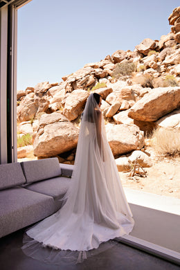 White wedding dress with a long flowing train and softly gathered floor-length skirt, viewed from behind