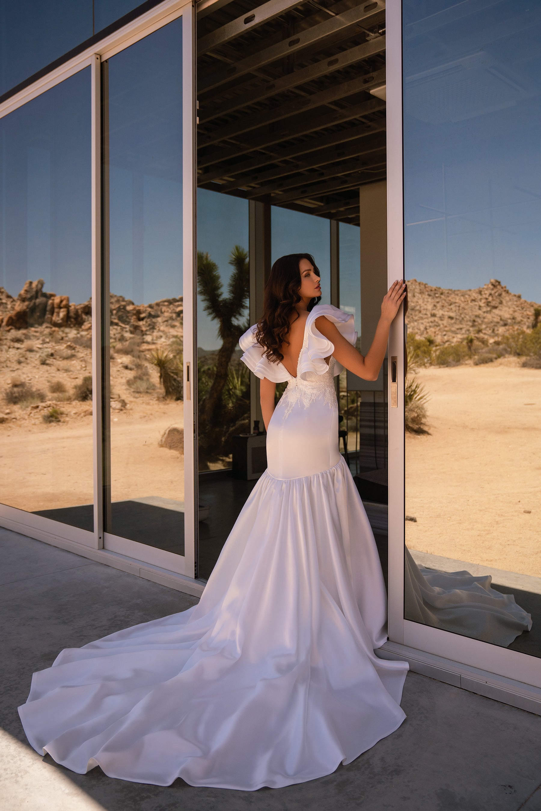 Back of a white mermaid wedding dress with ruffled sleeves and a long flowing train