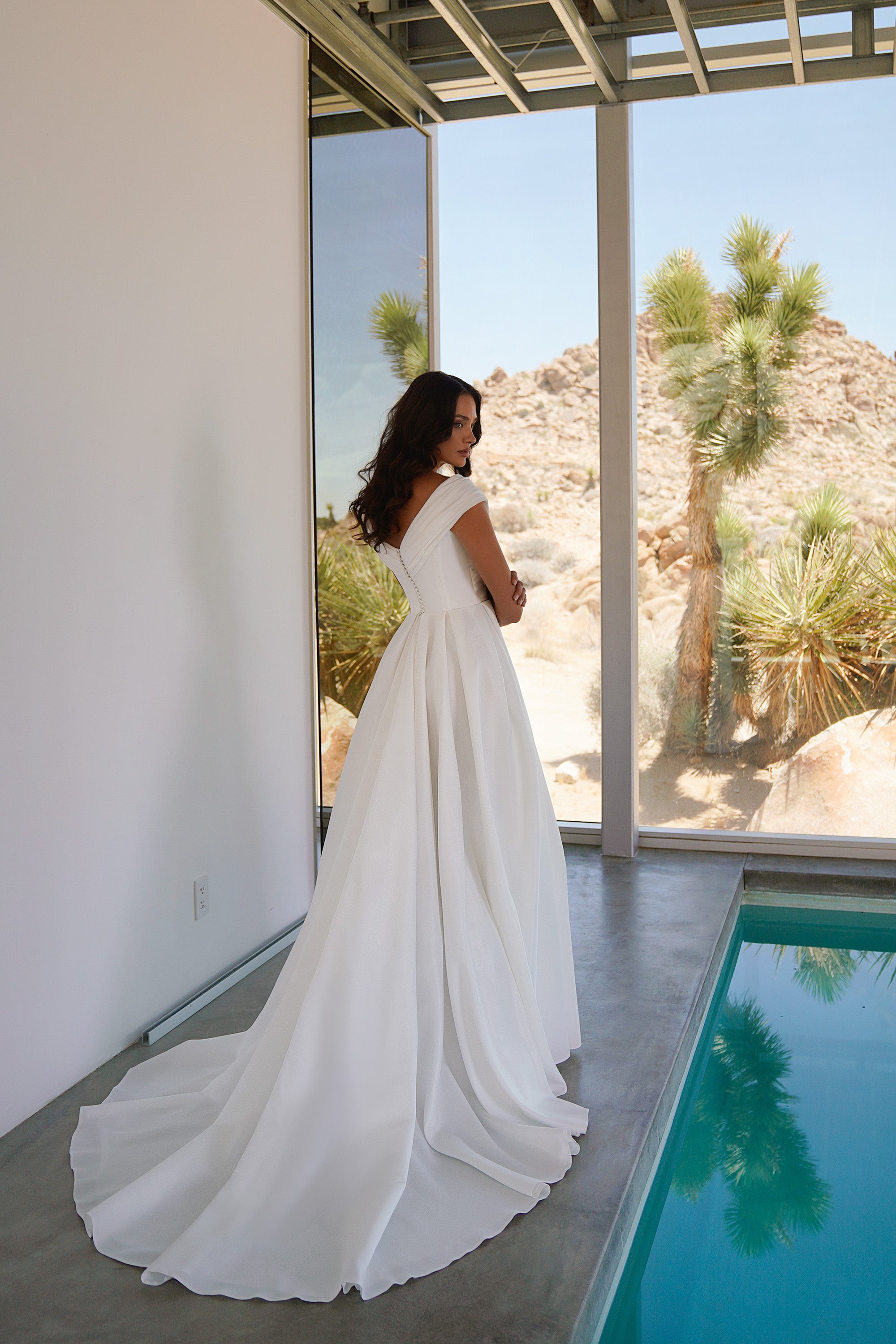 Ivory wedding dress showing a draped back neckline, fitted waist, flowing A-line skirt, and long train