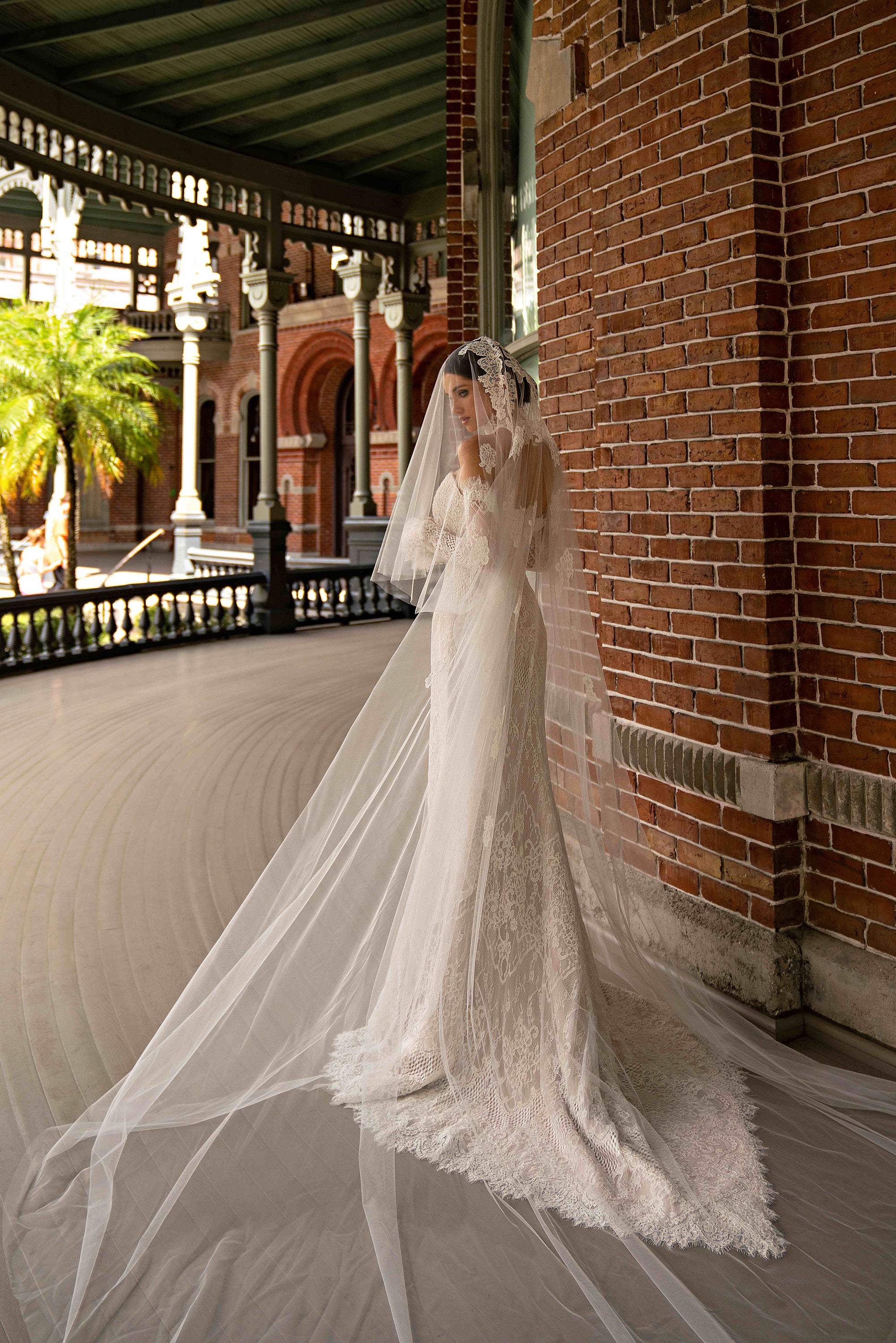 Side view of an ivory lace sheath wedding dress with a sheer overskirt and long trailing train