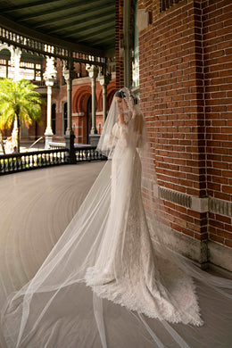 Side view of an ivory lace sheath wedding dress with a sheer overskirt and long trailing train