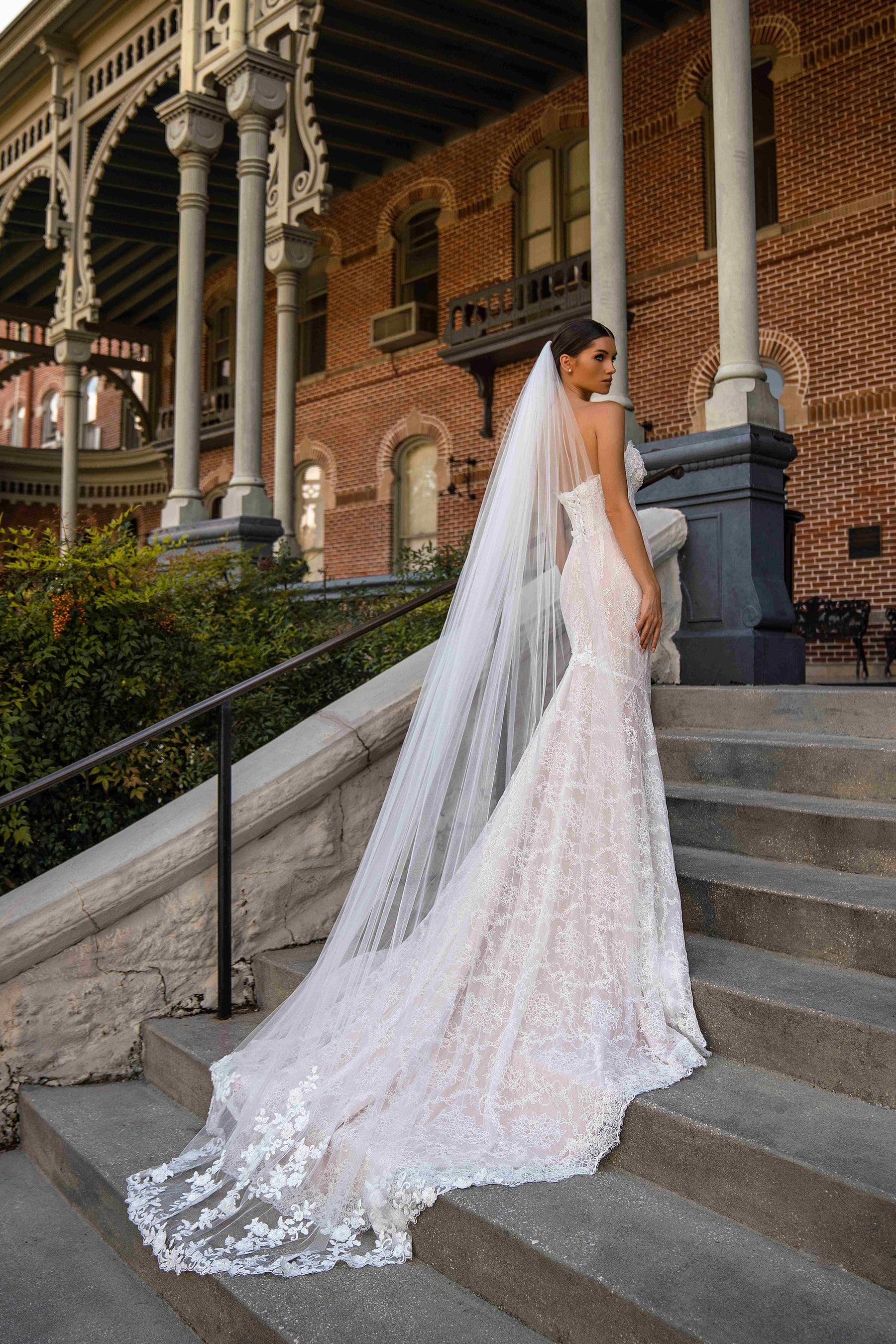 Ivory lace mermaid wedding dress shown from the back with a fitted silhouette and long scalloped train