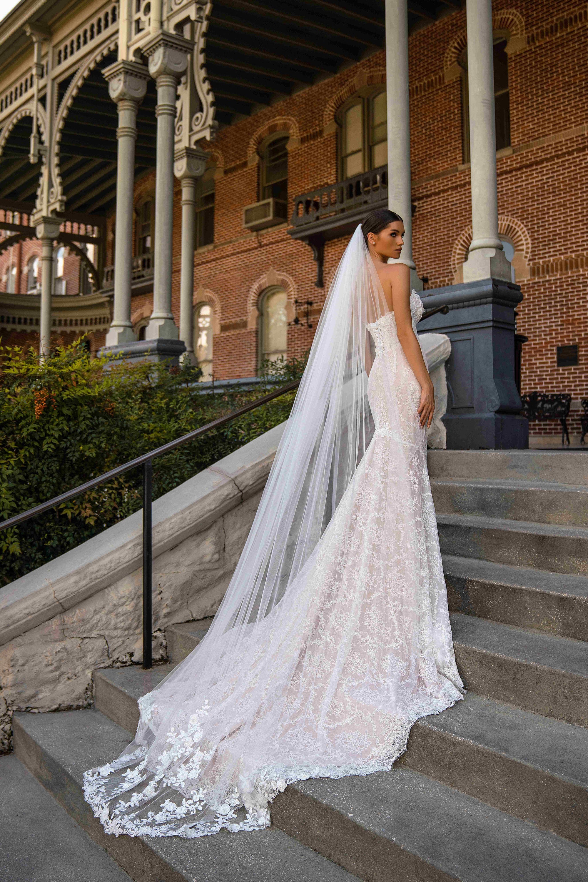 Ivory lace mermaid wedding dress shown from the back with a fitted silhouette and long scalloped train