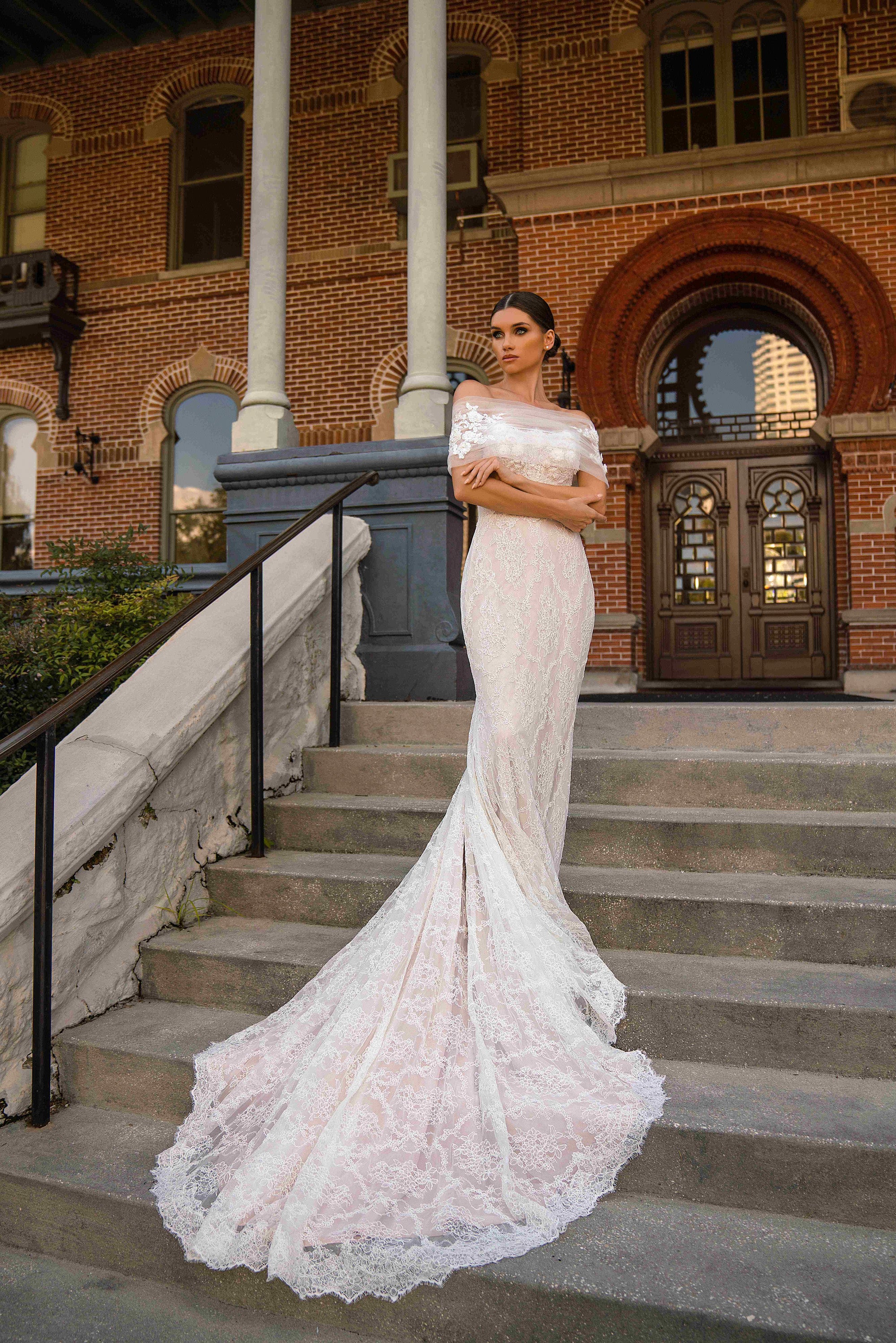 Ivory mermaid wedding dress with a sheer off-shoulder wrap, lace detailing, and scalloped train