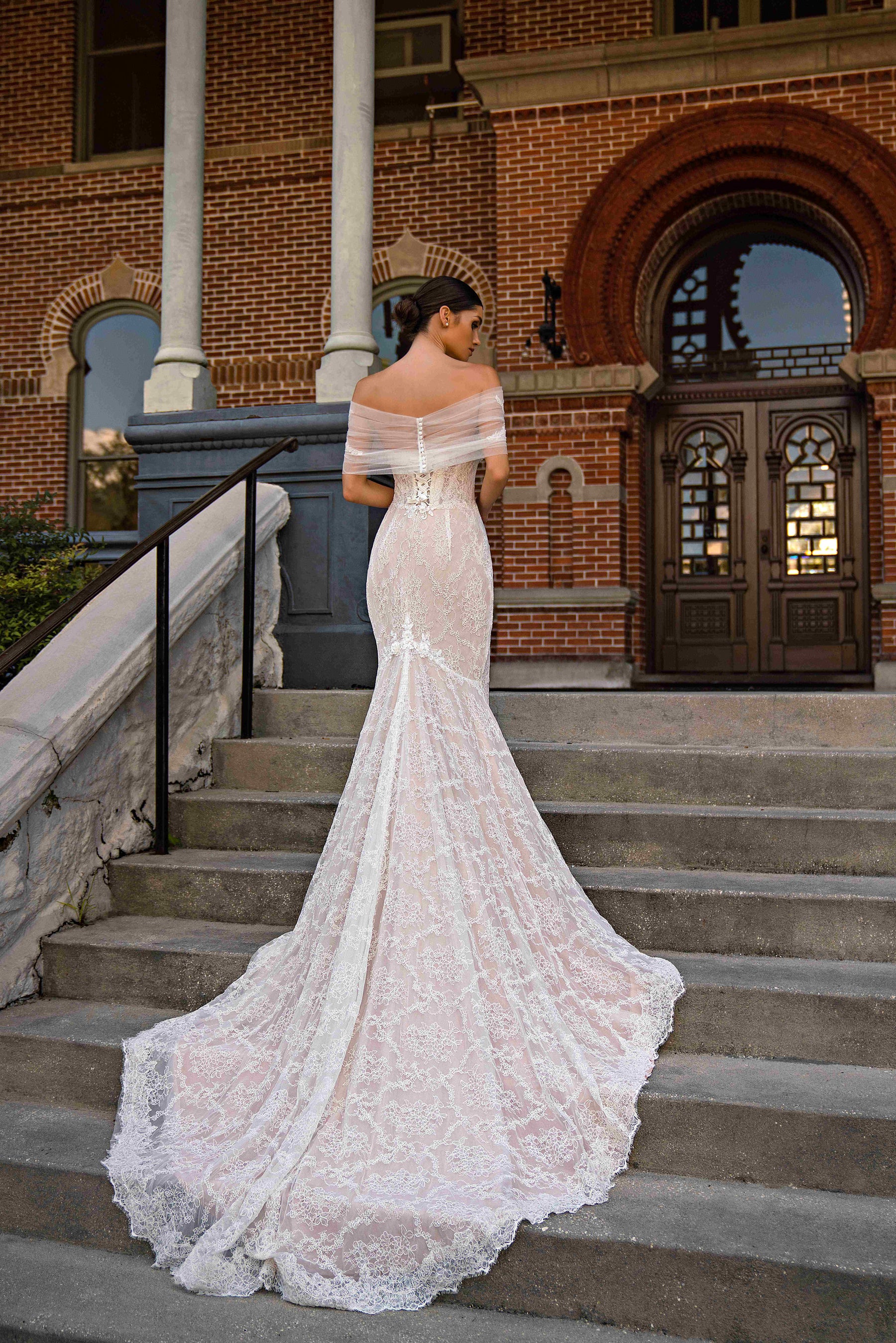 Back of an ivory lace mermaid wedding dress with a sheer off-shoulder wrap and long scalloped train