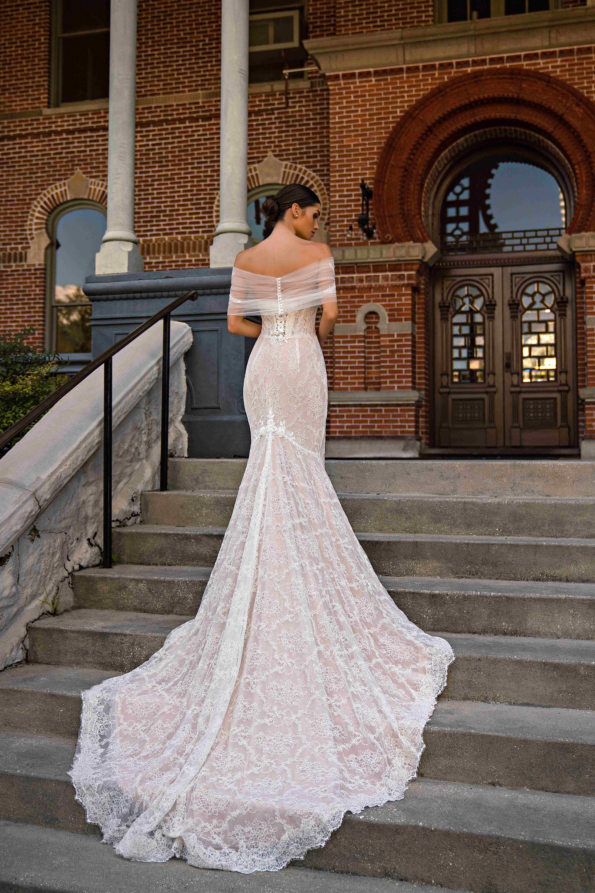 Back of an ivory lace mermaid wedding dress with a sheer off-shoulder wrap and long scalloped train