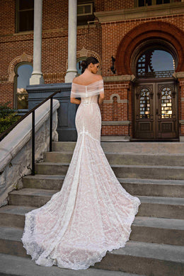 Back of an ivory lace mermaid wedding dress with a sheer off-shoulder wrap and long scalloped train
