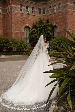 Side view of an ivory wedding dress with a full A-line skirt, long train, and long sheer lace sleeves