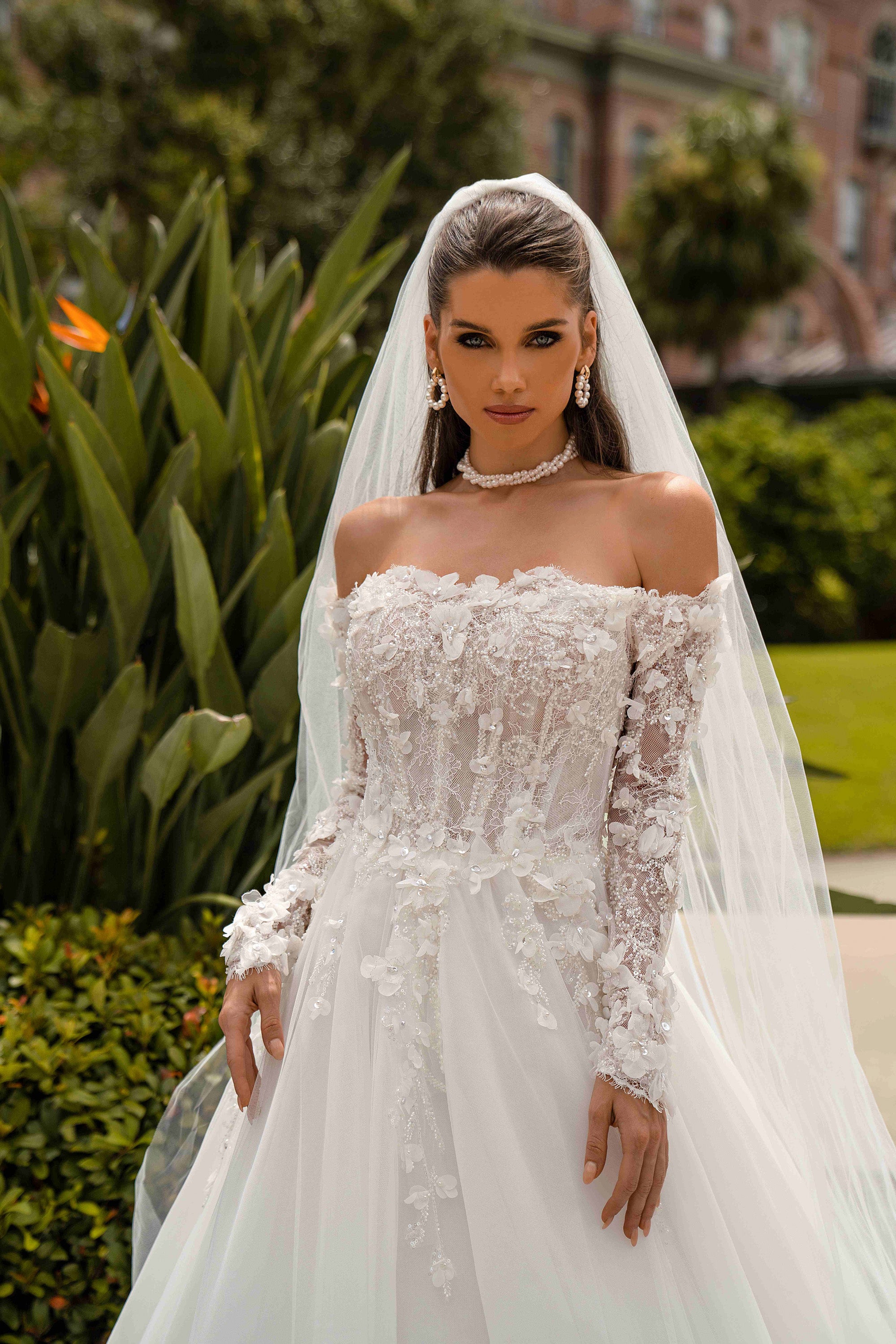 Close-up of an ivory wedding dress bodice with floral appliqués, beadwork, an off-the-shoulder neckline, and lace sleeves