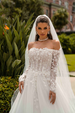 Close-up of an ivory wedding dress bodice with floral appliqués, beadwork, an off-the-shoulder neckline, and lace sleeves