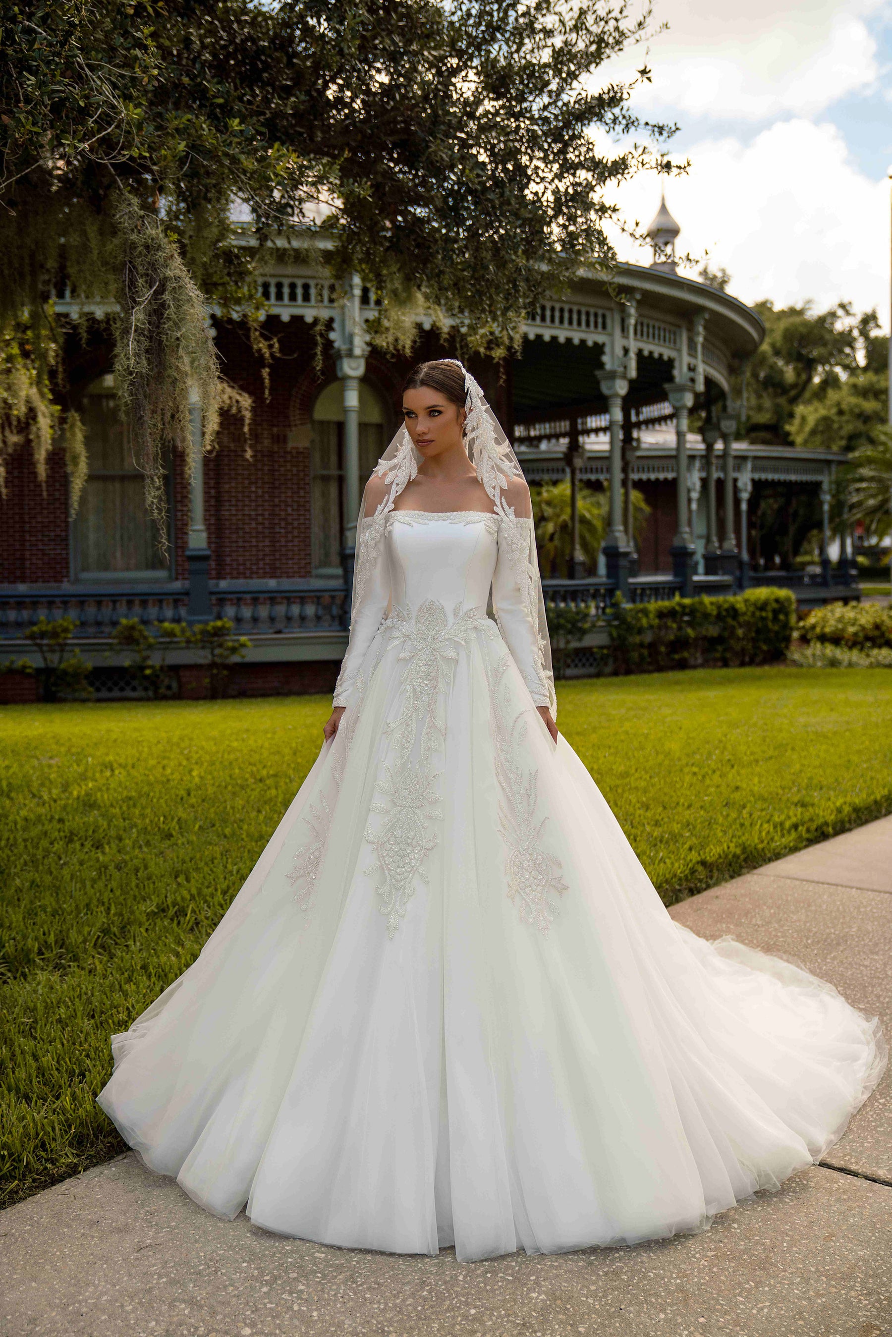 Ivory ball gown wedding dress with an off-shoulder neckline, long sleeves, floral appliqués, and a full tulle skirt