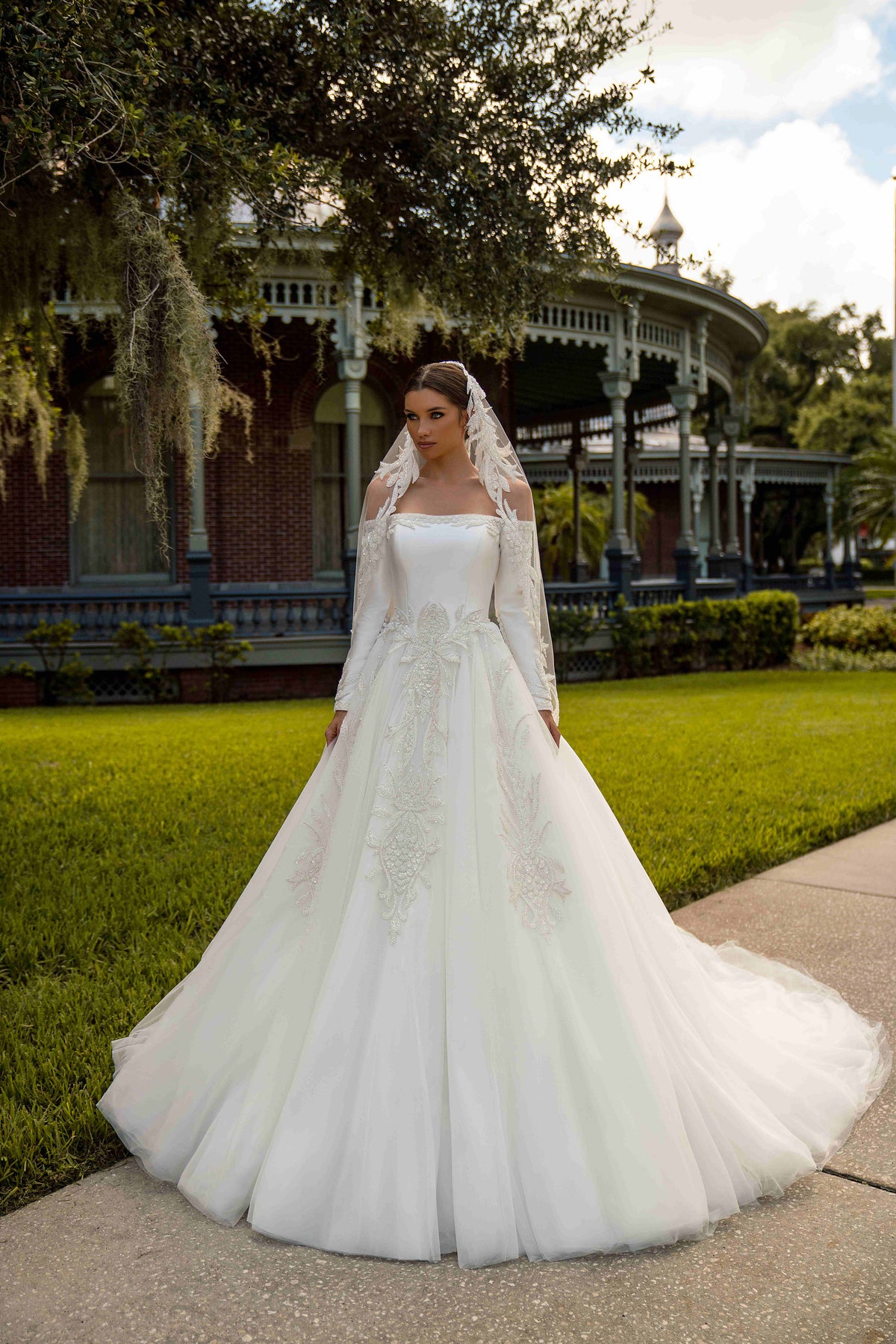 Ivory ball gown wedding dress with an off-shoulder neckline, long sleeves, floral appliqués, and a full tulle skirt