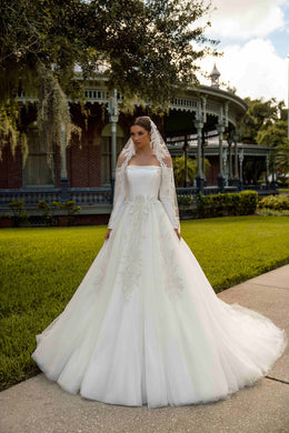 Ivory ball gown wedding dress with an off-shoulder neckline, long sleeves, floral appliqués, and a full tulle skirt